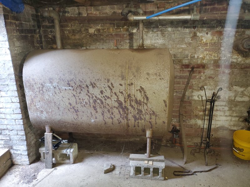 Old corroded steel oil tank with oil staining in a brick cellar before replacement